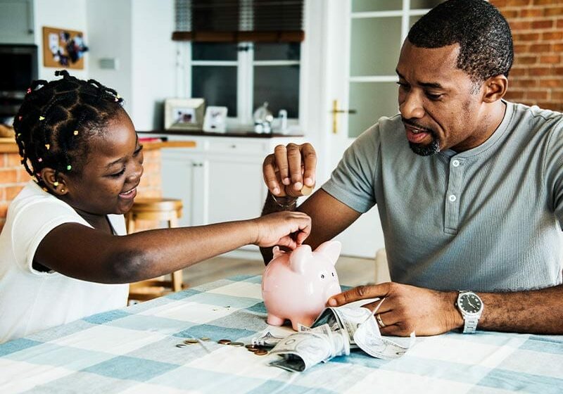 man and daughter putting money in piggy bank